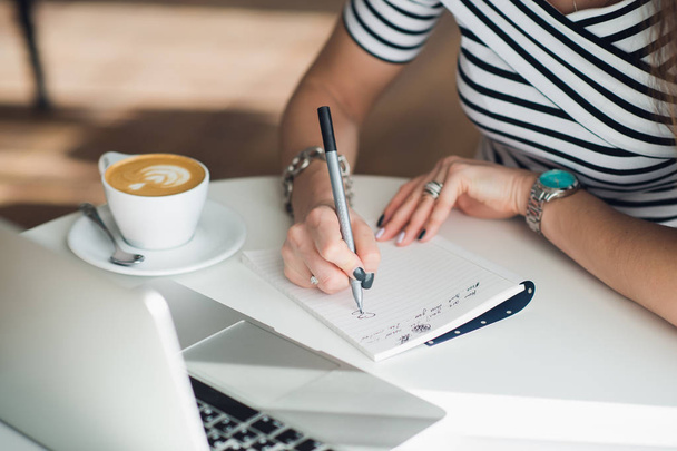 Un cuaderno blanco en blanco con un bolígrafo de lujo y una taza de café Latte con computadora portátil borrosa en el fondo
. - Foto, imagen