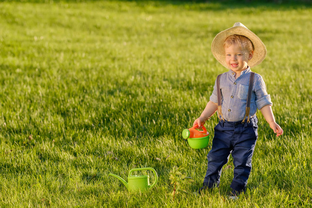 Маленький ребенок на свежем воздухе. Один год мальчик носит соломенную шляпу с помощью лейки
 - Фото, изображение