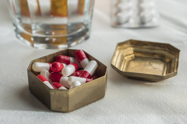 Metalen pillendoos met witte en rode capsules samen met waterglas - Foto, afbeelding