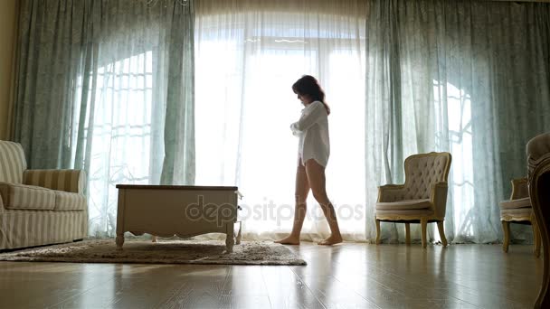 Αναστατωμένος γυναίκα σε πουκάμισο πηγαίνοντας εμπρός και πίσω κατά μήκος το παράθυρο από ένα άνετο διαμέρισμα - Πλάνα, βίντεο