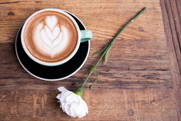 Hot mocha coffee or capuchino with heart pattern and white carnation flower on the wooden table - Photo, Image
