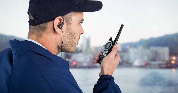Security guard with cap and walkie talkie against blurry skyline - Фото, изображение