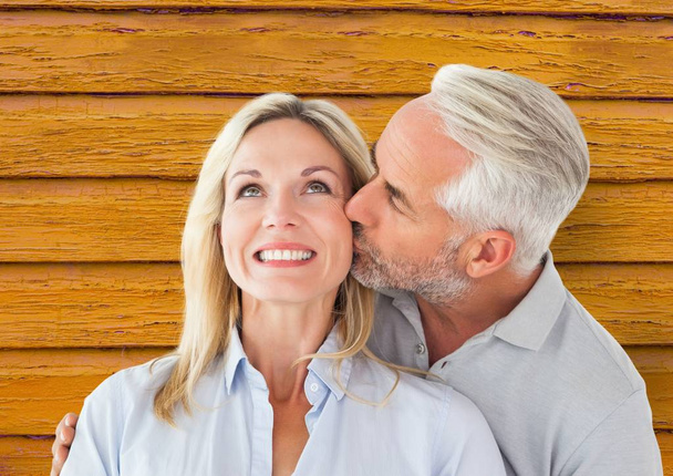 couple: man giving kiss to the woman with yellow wood background - Foto, Imagen