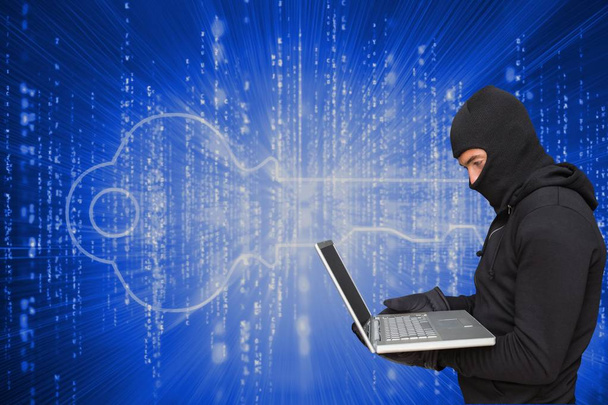 Cyber criminal wearing an hood is hacking a laptop against matrix code background - 写真・画像