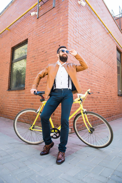 Молодой стильный мужчина с бородой в солнечных очках сидит на велосипеде на кирпичном фоне
 - Фото, изображение
