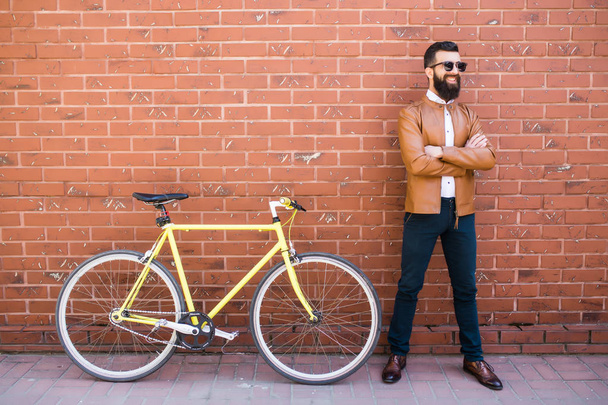 Красивий молодий бородатий чоловік стоїть біля свого велосипеда на цегляній стіні
 - Фото, зображення