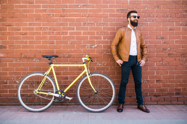 Красивий молодий бородатий чоловік стоїть біля свого велосипеда на цегляній стіні
 - Фото, зображення