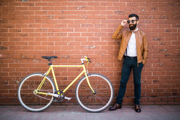 Красивый молодой бородатый мужчина, стоящий возле велосипеда у кирпичной стены
 - Фото, изображение