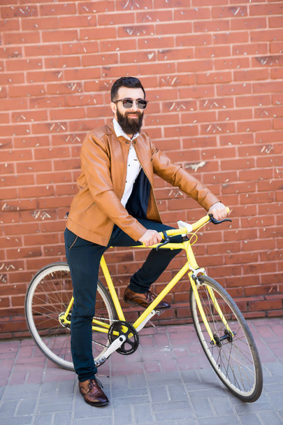 Fresco giovane hipster barbuto oltre a una bicicletta fixie sul muro di mattoni sulla strada
 - Foto, immagini