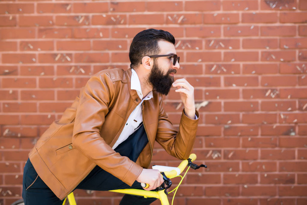 Joven hombre guapo con barba contra pared de ladrillo se sienta en una bicicleta
 - Foto, imagen