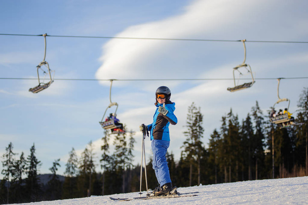 Female skier against ski-lift and forest on a sunny day - Photo, Image