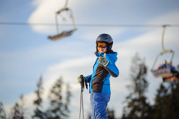 Mulher esquiadora contra ski-lift e floresta em um dia ensolarado
 - Foto, Imagem