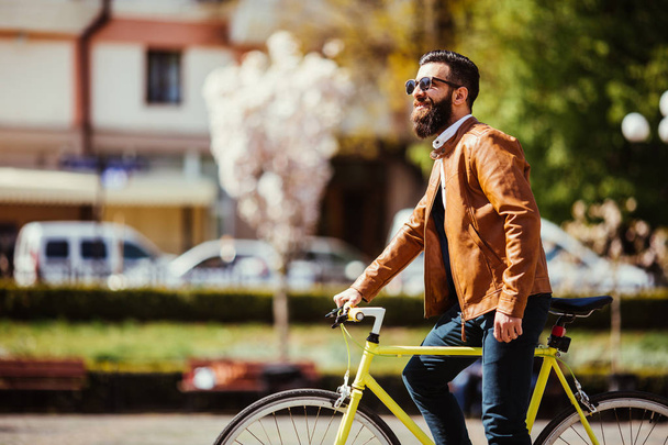 Um jovem hipster elegante posando ao lado de sua bicicleta na rua da cidade
 - Foto, Imagem