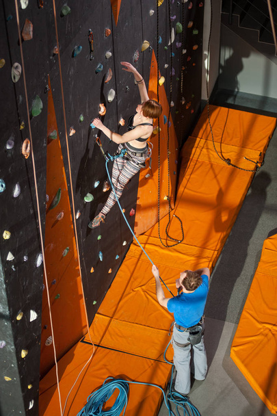 Альпинистка взбирается на крытую скалолазание стену
 - Фото, изображение