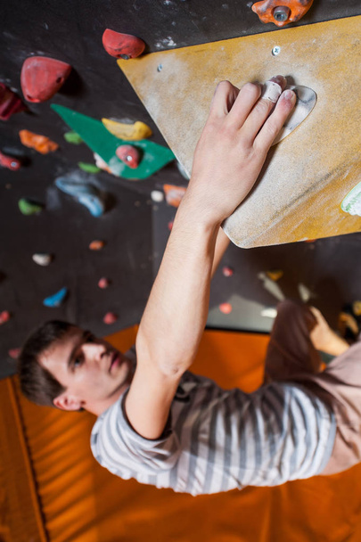 Strong male climber on boulder climbing wall indoor - Foto, afbeelding