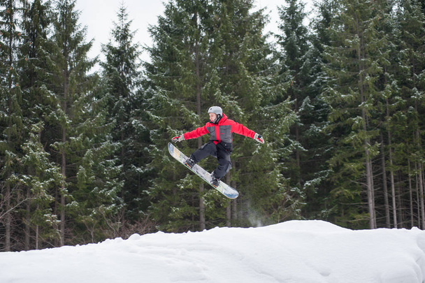 Boarder masculino en la tabla de snowboard saltando sobre la pendiente
 - Foto, Imagen