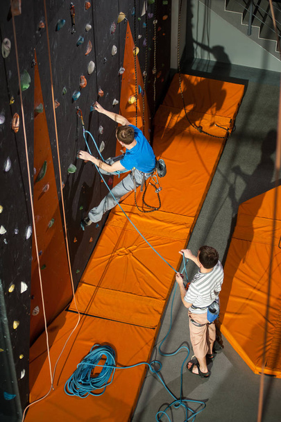 Male rock-climber practicing climbing on rock wall indoors - Фото, изображение
