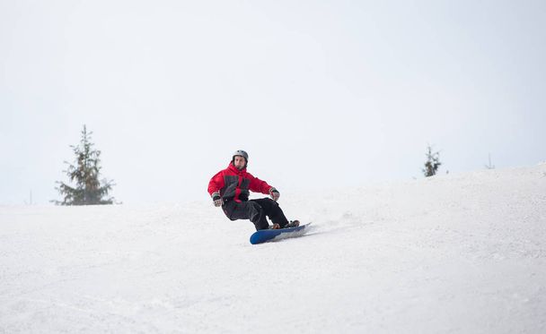 Male snowboarder riding down from the mountain in winter day - Photo, Image