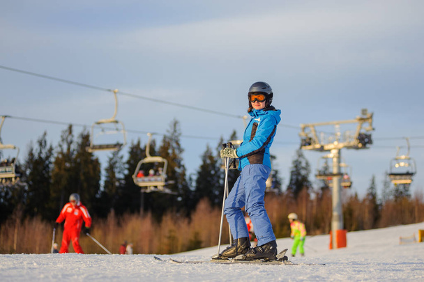 Female skier against ski-lift and forest on a sunny day - Photo, Image
