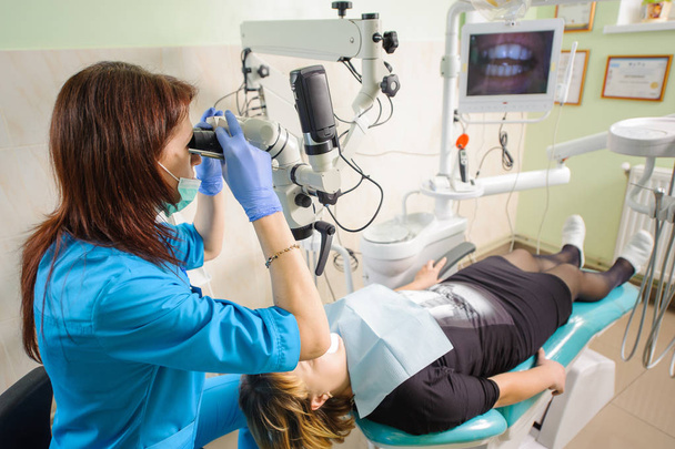 Γυναίκα οδοντίατρος εργάζεται με μικροσκόπιο στο σύγχρονο οδοντιατρείο - Φωτογραφία, εικόνα