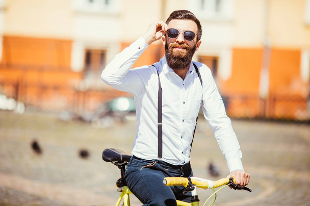 Handsome hipster in sunglasses enjoying city ride by bicycle. - Фото, изображение