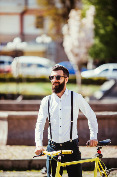 Jonge stijlvolle bebaarde man met een fiets fixie op zonnige straat - Foto, afbeelding