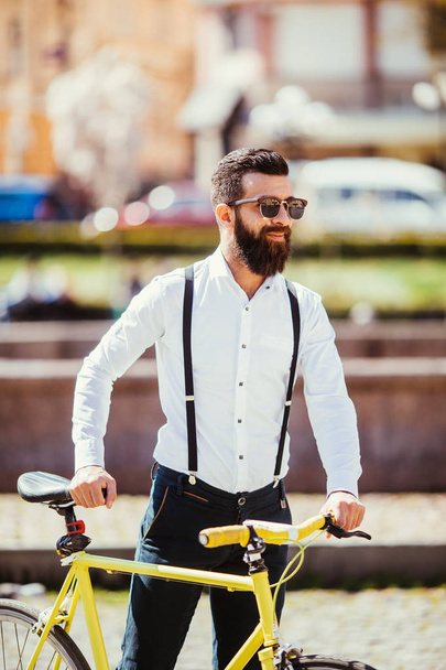 Молодой стильный мужчина едет на работу на велосипеде. хипстер с велосипедом на улице. бородатый человек смотрит в сторону, когда едет на велосипеде на открытом воздухе
 - Фото, изображение