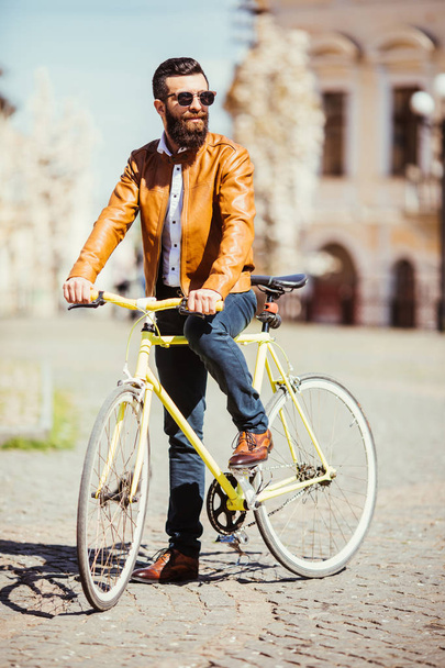 Pohledný vousatý mladý muž v sluneční brýle na kole ve městě. Koncept kol - Fotografie, Obrázek