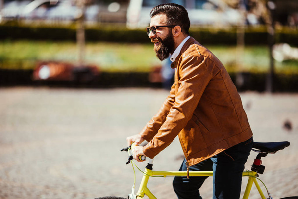 Молодий бородатий чоловік їде на велосипеді на вулиці на сонячній вулиці
 - Фото, зображення