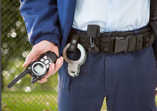 security guard with walkie-talkie on his hand and cuffs on the belt in front of the fence - Fotoğraf, Görsel