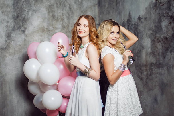 Blonde and redhead. Two young charming girlfriends at the party with balloons. On gray textured background - Foto, immagini