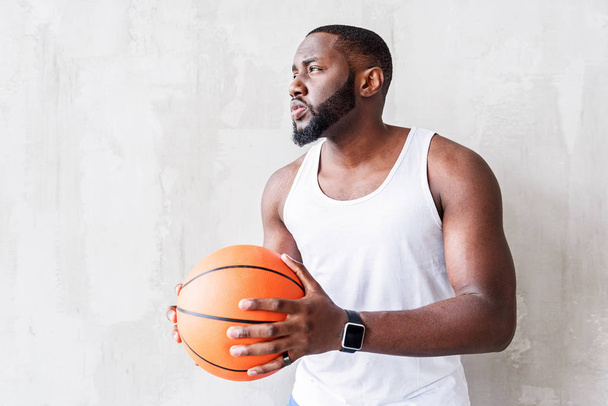 Pensive attractive sportsman standing by wall with ball in his arms - 写真・画像