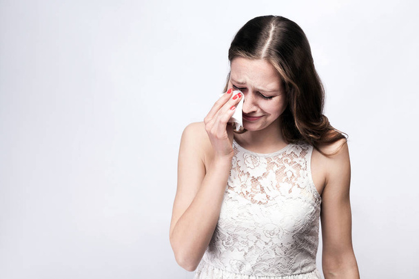 Portrait of sad, unhappy crying woman with freckles and white dress and smart watch on silver gray background. copy space. healthcare and medicine concept. - Photo, image