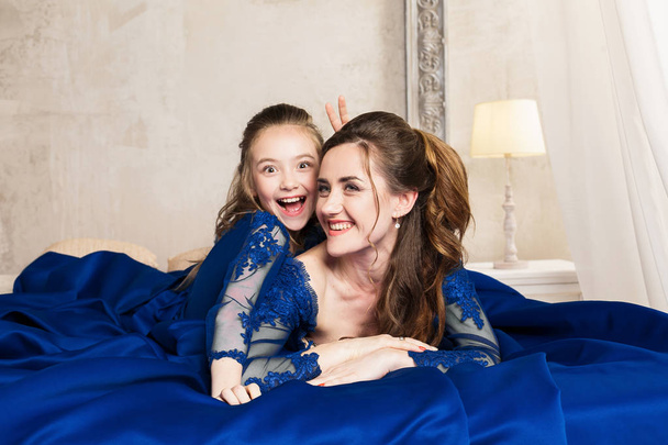 Mother and daughter hugging and looking at the camera. Happy loving family. Mother and daughter in beautiful long luxury blue dresses, makeup hairstyle. Fashion family portait. Generation relationship - Photo, Image