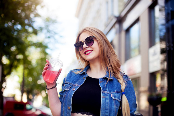 Cool girl with long hairstyle and red lips having fun in the city. She wears sunglasses and smiling to camera - Fotoğraf, Görsel