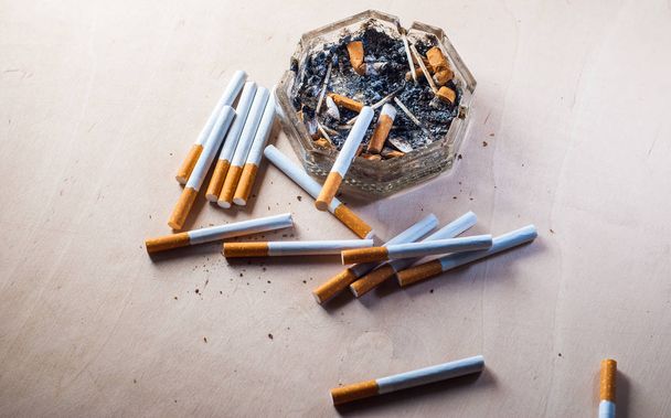 Un cenicero sucio con colillas de cigarrillos esparcidos cigarrillos de filtro en una mesa de madera
, - Foto, Imagen