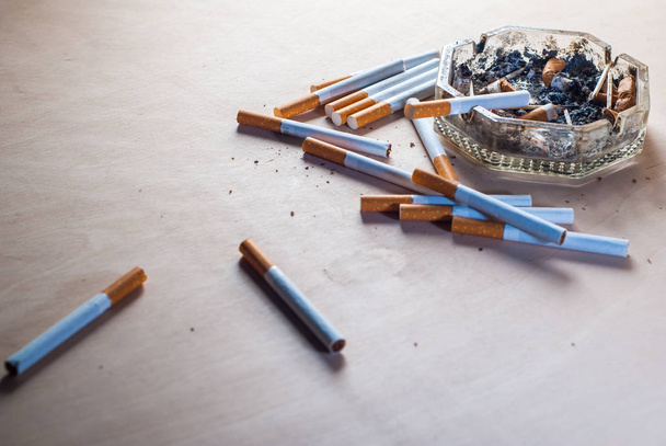 Un cenicero sucio con colillas de cigarrillos esparcidos cigarrillos de filtro en una mesa de madera
, - Foto, imagen