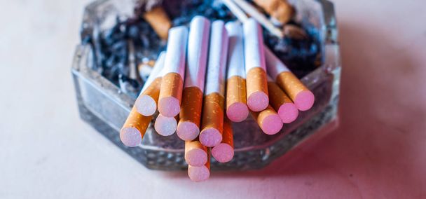 Een stelletje gefilterde sigaretten in een vieze asbak met sigaretuiteinden, - Foto, afbeelding