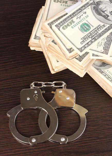 Handcuffs and packs of dollars on wooden table close-up - Fotó, kép