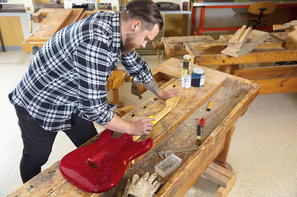 Craftsman sanding a guitar neck in wood at workshop - Фото, изображение