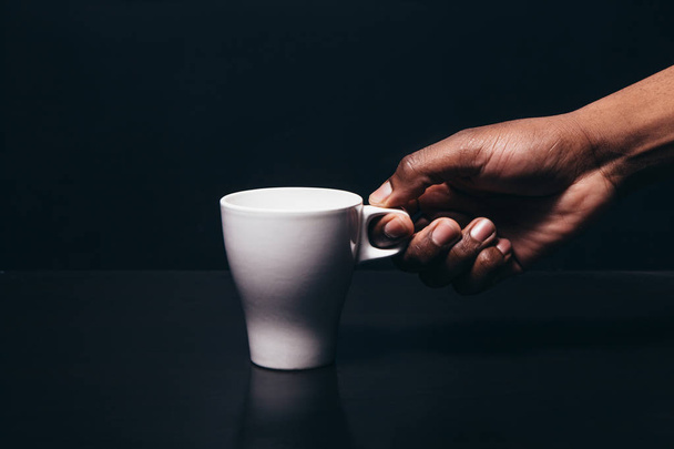 Black man hand take white cup, dark background - Foto, Imagen