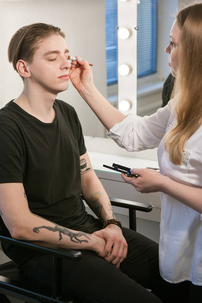 Beautician applying cosmetics on mans eyes - 写真・画像