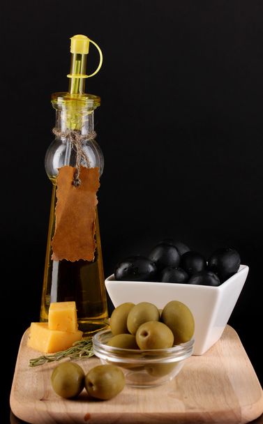 Black and green olives in bowl with rosemary,olive oil and cheese on board isolated on black - Photo, Image