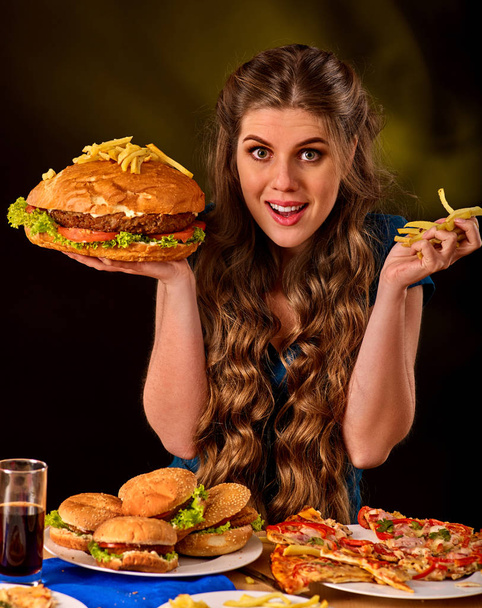 Woman eating french fries and hamburger on table. - Zdjęcie, obraz