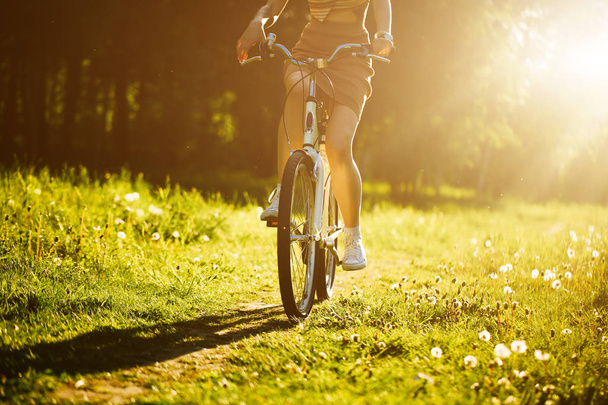 Funny girl driving bicycle outdoor. Sunny summer lifestyle concept. Woman in dress and hat in Field with dandelions. Female ride in park. Light photo effect for text. Copyspace for design. - Фото, зображення