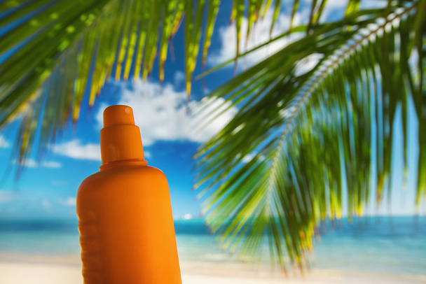 Botella de loción de protección solar y hoja de palma en el fondo
 - Foto, imagen