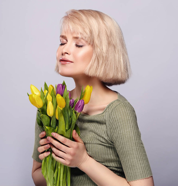 Beautiful young blonde girl breathes the scent of spring flowers - Zdjęcie, obraz
