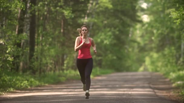 jonge vrouw joggen in zomer bos. het meisje gaat in voor sporten in de natuur. het model loopt naar de camera. - Video