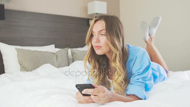 Sexy woman in a shirt lies on a bed, kicking feet and dreaming - Felvétel, videó