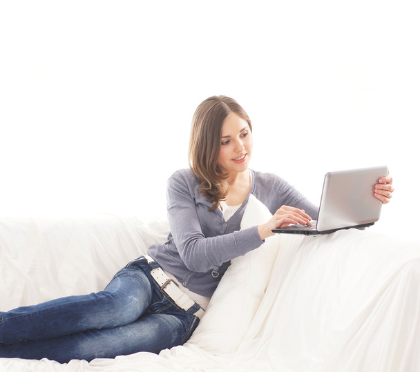 Young attractive girl with the laptop sitting and relaxing on the sofa - Photo, image